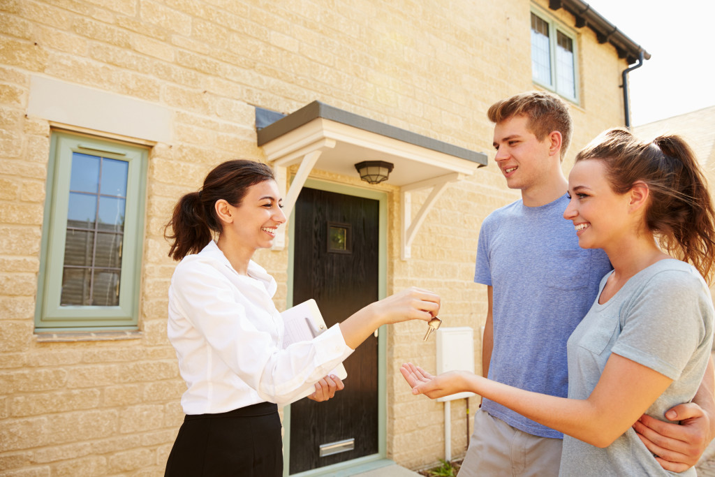 young landlord handing keys to new tenants couples